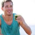 Smiling man wearing muscle shirt holds a cup of green health drink