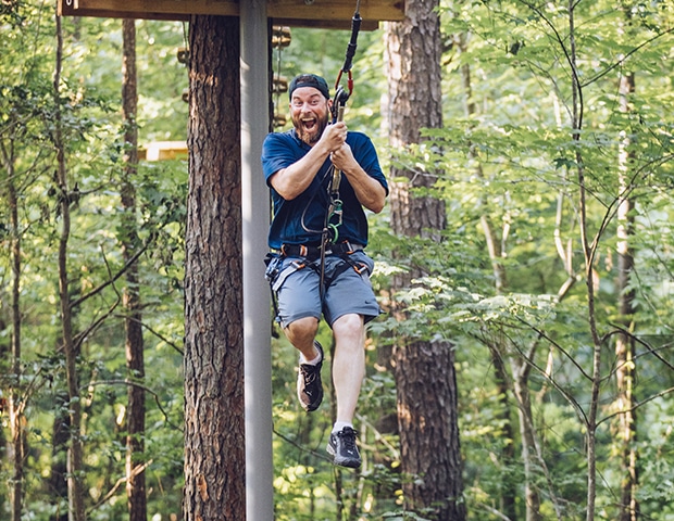 Excited man grips his safety lines after stepping off wooden platform to swing on Tarzan swing