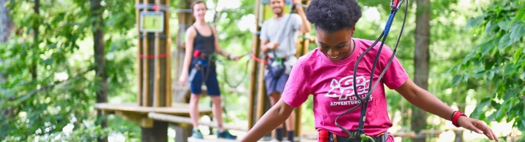 Three young adults balancing on a high ropes obstacle at Go Ape Treetop Adventure