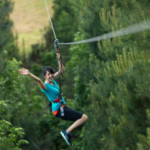 Young woman in blue shirt waves happily from a zipline