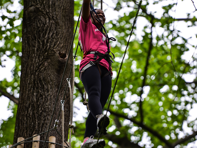 A woman climbs across a bridge in the treetops