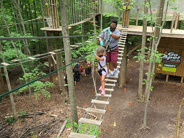 A parent and child climb across a bridge together