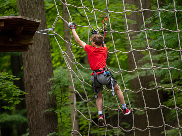 Boy in red climbs net after Tarzan swing
