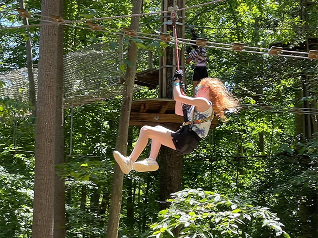 A girl ziplines through the forest