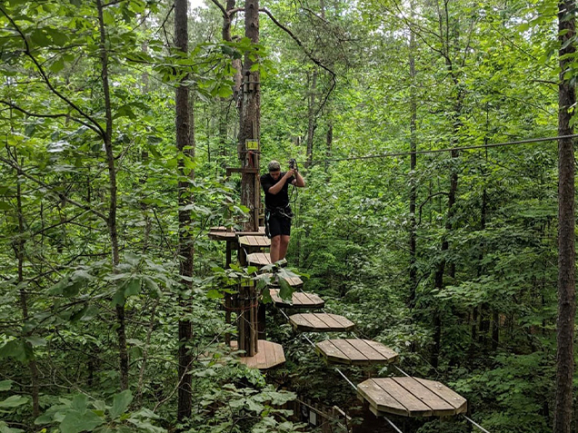 A climber crosses treetop bridge at Go Ape outdoor adventure ropes course Williamsburg