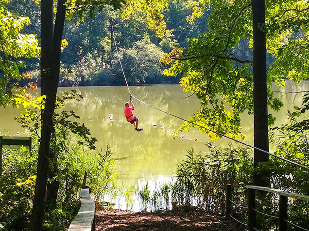 Zipliner in red zips above the lake