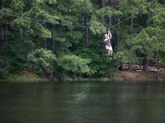 Young woman ziplines above a lake