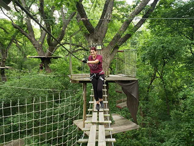 Woman crossing obstacle on Go Ape outdoor adventure ropes course plano