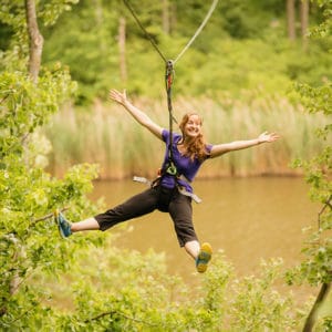 Adult with purple shirt smiling on a zipline