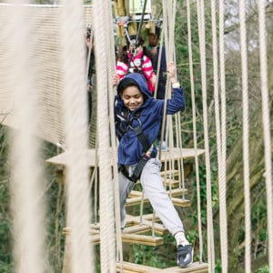 young boy in blue smiling on a treetop obstacle crossing