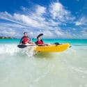 Two people ride a kayak through ocean waves near the shoreline