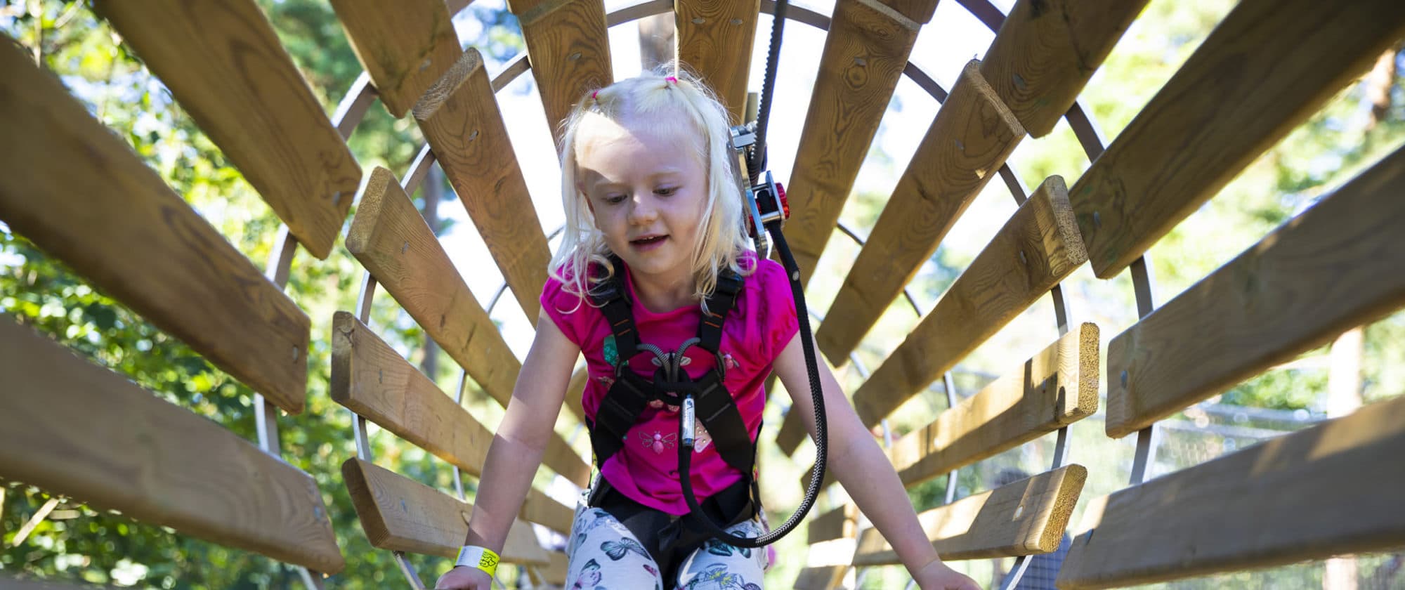 Little girl having fun as she crawls through a barrel obstacle at a Go Ape Treetop Journey