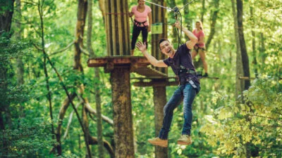 Smiling man waves at the camera while riding a zipline away from a wooden platform