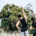 Young man and woman do yoga poses in a grassy field