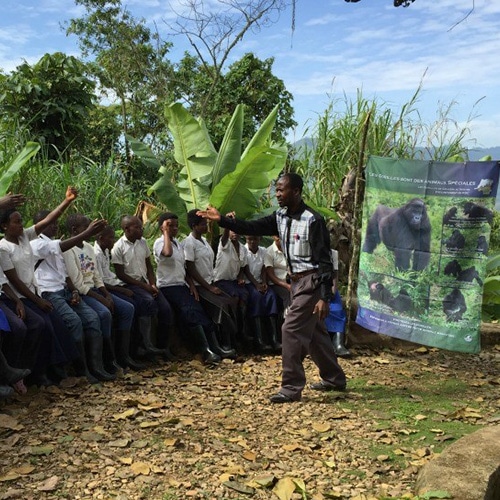 Man gestures with his hands while teaching schoolchildren in front of a banner with info on gorillas