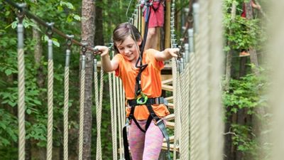 Small girl holds on to guiding ropes while navigating treetop obstacle