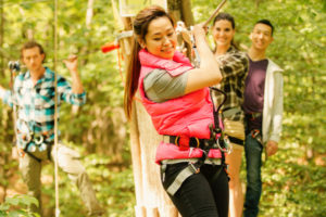 A woman climbs with friends watching from the platform behind her