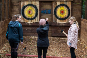 Group of three young women prepare to throw axes at a target