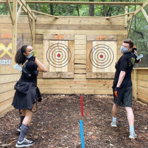 Two people wind up to throw axes at a target